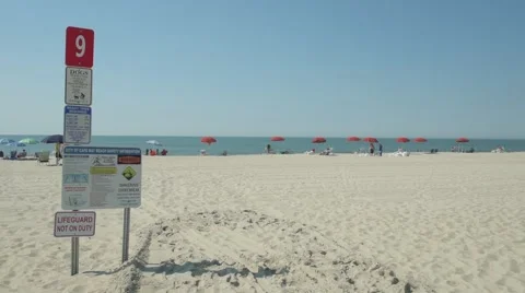Tilt up to reveal beach warning sign with umbrellas and sea in distance. Stockbeeldmateriaal 64355778