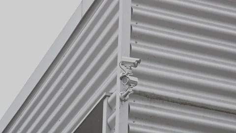 Tilt up to security cameras on the corner of a metal plated warehouse Stock Footage 319513310