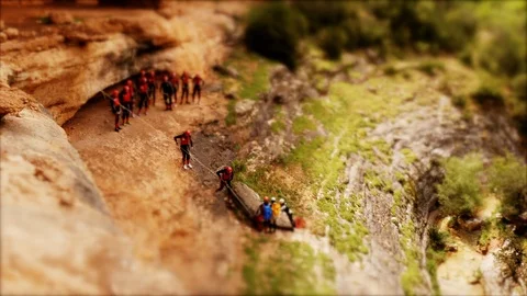 Tilt-shift: Miniature Canyoning group climing down single file to abseiling spot Stock Footage 98235909