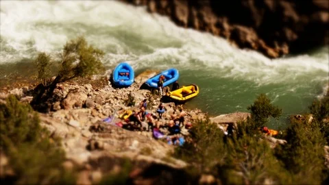 Tilt shift: Miniature man pumping up a raft at the river -wide shot Stock Footage 98306213