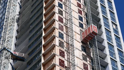 Tilt shot of a construction crane moving beside a high-rise building 스톡 동영상 219778926