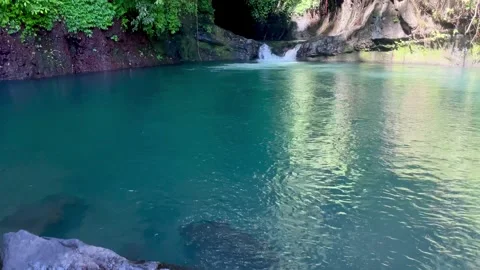 Tilt up shot of a crystal clear emerald lagoon and hidden cave waterfall in Bali Stock Footage 336904302