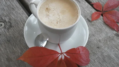A tilt shot of a cup of coffee with red leaves on a wooden table. Stock Footage 142543423