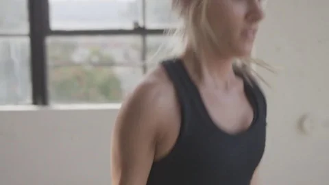 Tilt up shot of young athlete skipping with jumping rope by window at gym Stock Footage