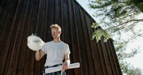 Tilt up view of young man putting on hardhat and starting to read draft while Stock Footage 141463454