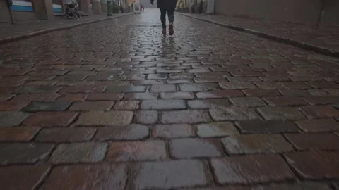 Tilt up of woman walking down an empty, wet cobbled street in Helsinki, Finland Stock Footage 146291232