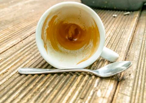 Tilted dirty empty espresso cup on a wooden table with coffee crema and spoon Foto stock