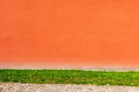 Tilted orange bricks wall texture with grass and sidewalk background. Stock Photos
