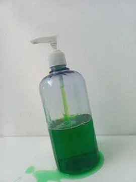 Tilted Plastic Soap Pump Bottle with Green Liquid Spilled on White Table Stock Photos