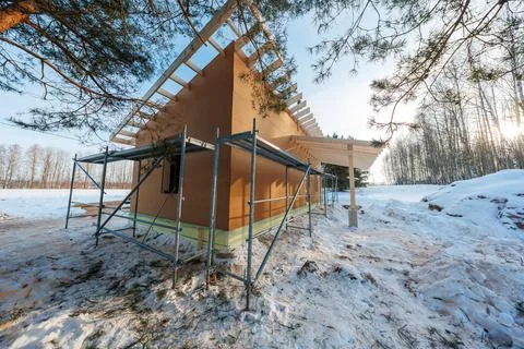 Timber frame cabin under construction in a snowy forest clearing Stock-Fotos