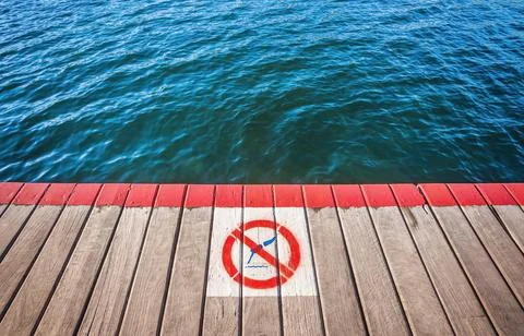 Timber walkway with No Diving caution sign over blue water Stock Photos