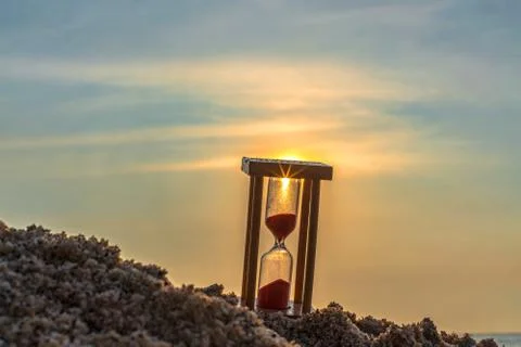 Time concept Hourglass on sandy beach in summer with sea background Stock Photos