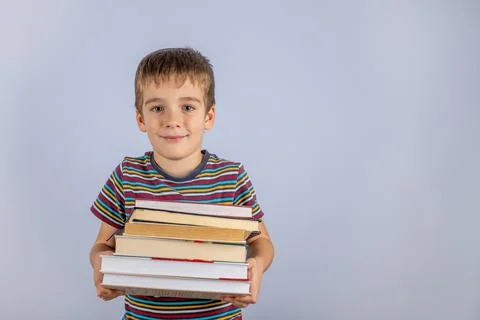 Time To Explore The Concept. A small novice schoolboy holding a stack of book Stock Photos