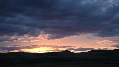 Time lapse of blue, orange, and purple clouds moving above dark hills Stock Footage 241099921