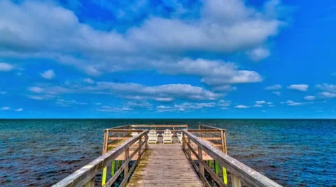 Time-lapse blue sky cloudscape of pier with white beach chairs - HD Stock Footage 7745908