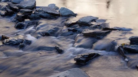 Time lapse of blurry water flowing over river rocks on a sunny afternoon Stock Footage 73339730
