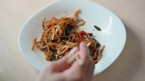 Time-lapse close-up of a man eating noodles with chopsticks from a white plate 動画素材 338186572