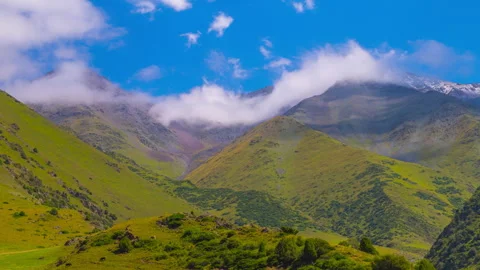 Time-lapse of clouds flow on blue sky above green mountains in Kyrgyzstan at Stock Footage 335990542