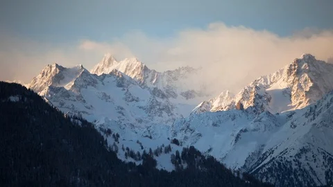 Time-lapse of clouds moving above snow covered mountains during sunrise Stock Footage 116742724