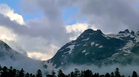 Time lapse of clouds rising from snowy high mountains and forests in sunset Stock Footage 65773920
