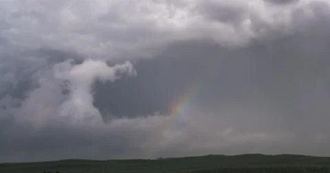 Time-lapse clouds swallowing up a rainbow in a gray sky over the prairie Video stock 59328216