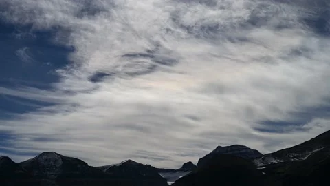 Time lapse of curving white clouds in a dark blue sky above a range of mountains Stock Footage 219863805