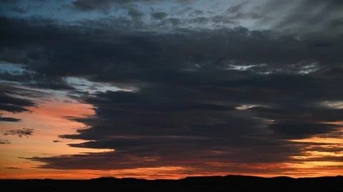 Time lapse of dark clouds in an orange sunset sky with distant silhouetted hills Stock Footage 286902734
