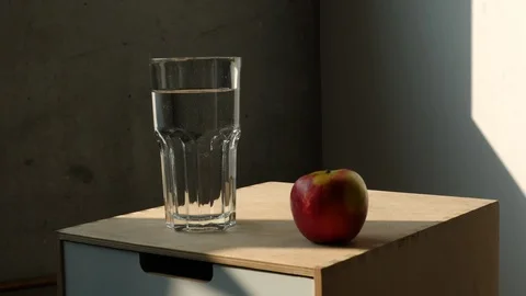 Time Lapse of Daylight over Red Apple and Glass of Water on Nightstand Stock Footage 113875897