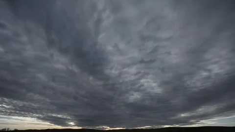 Time lapse of dramatic gray storm clouds moving above distant rolling hills Stock Footage 306541752