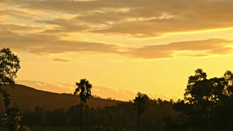 Time-lapse of golden clouds rolling over distant mountain range during sunset Stock Footage 235892329