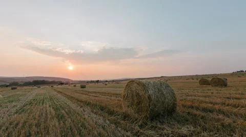 Time-lapse of golden sunset over farm field with hay bales Видео 66296090