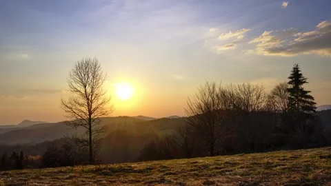 Time lapse of golden sunset over mountain ridge with trees in foreground Stock Footage 336395242