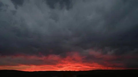 Time lapse of gray clouds above a red sunset behind a skyline of small hills Stock Footage 296657157