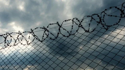 Time lapse, gray clouds flying over fence of prison. Stock Footage 92378589