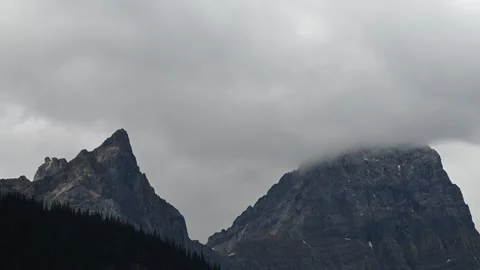 Time lapse of gray rain clouds moving above rugged rocky mountains with trees in Stock Footage 297004355