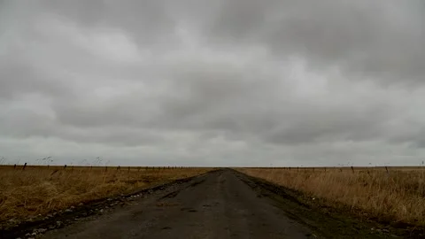 Time lapse of gray storm clouds blow rapidly over a dirt road and field of grass Stock Footage 153555726
