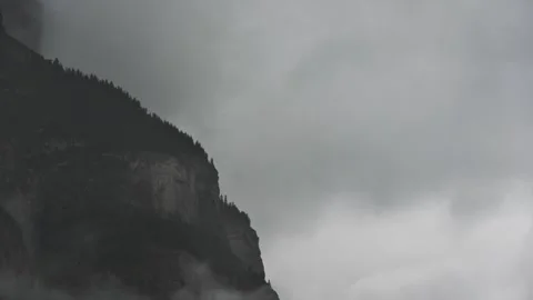 Time lapse of light to dark gray misty clouds swirling next to a foggy rocky mou Stock Footage 290437779
