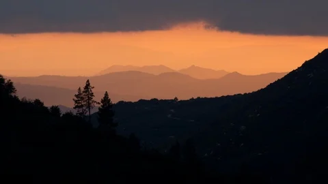 Time lapse long shot of silhouetted trees on a mountain ridge at sunset Stock Footage 98908439