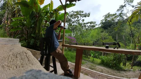 Time lapse of man sits on a rustic porch using camera to watch and capture .. 動画素材 338203911