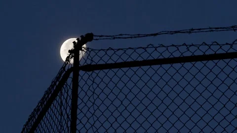 Time Lapse. Moon Behind Barbed Wire Fence At Night Over Chain Link Silhouette Video stock 320288432