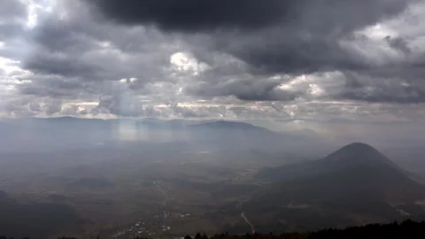 Time lapse from mountain peak as sun rays break through clouds above a cone Stock Footage 333831489