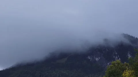 Time-lapse movement of fast clouds across a misty alpine mountain peak. Zoom in 動画素材 217396007
