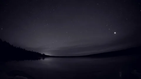 Time lapse of the night sky above a frozen lake with stars slowly moving and a r Stock Footage 321199350