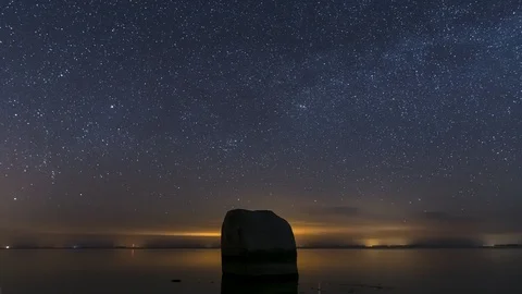 Time lapse of the night sky with the ocean and a huge boulder in the forground Video stock 127446917