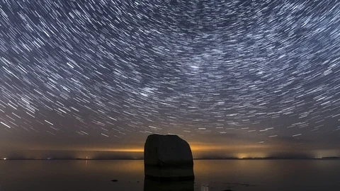 Time lapse of the night sky with star trails and the ocean with a huge boulder Stock Footage 127436656