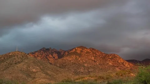 Time lapse of an orange sunset glow and rain clouds over desert peaks Stock Footage 348509384
