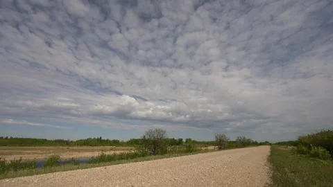 Time lapse of puffy white clouds moving towards the viewer above a gravel road Stock Footage 249838269