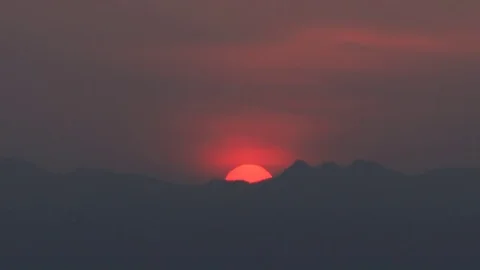 Time lapse of rising red sun through dark blurry clouds over mountain Stock Footage 73754296