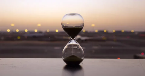 Time-lapse of sand flowing in hourglass by airport window at sunset Stock Footage 346522516