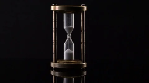 Time Lapse of Sand Flowing Through vintage metal hourglass on black background Video stock 75964771